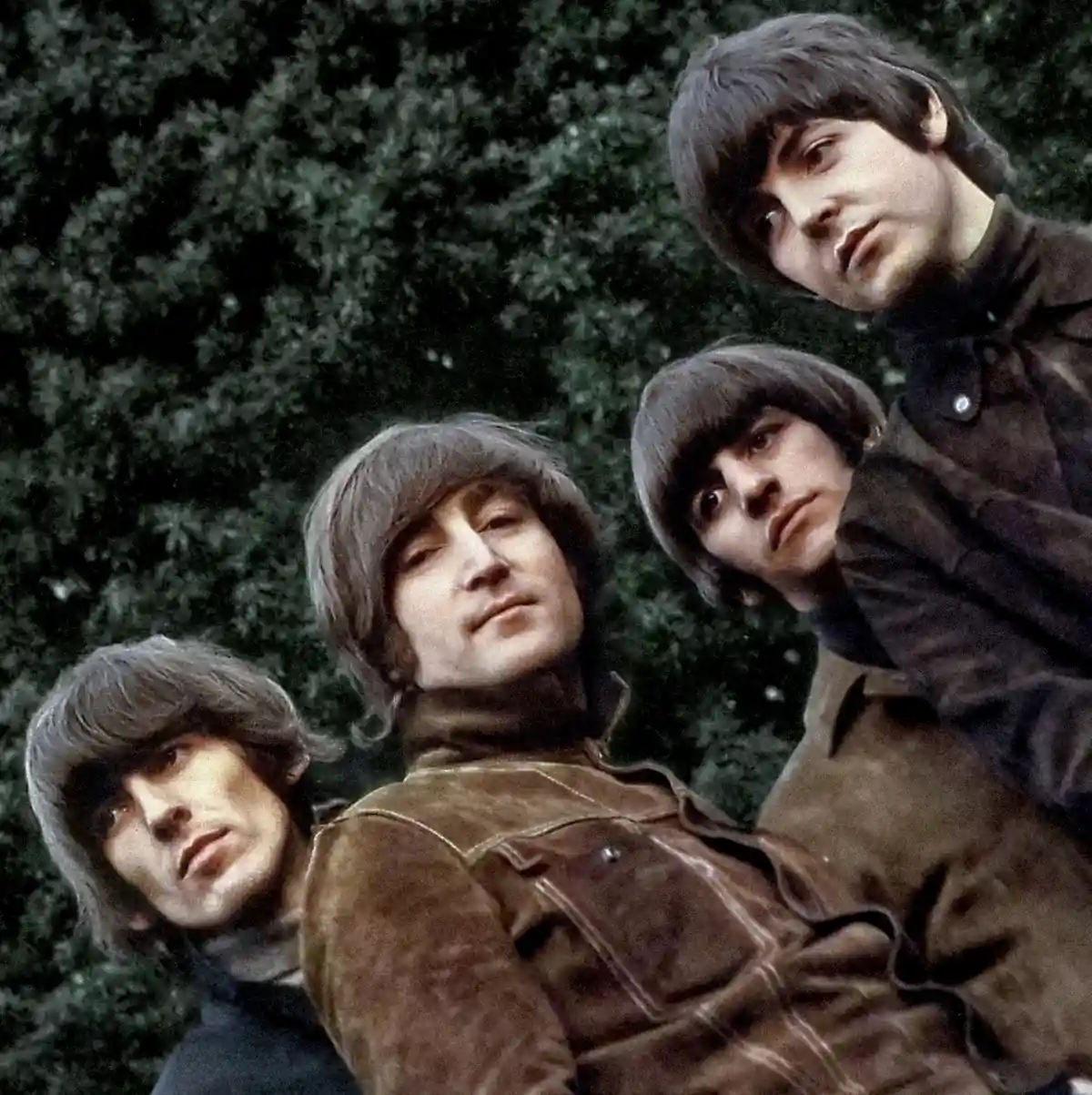 A vintage photograph of the four members of The Beatles looking directly at the camera with serious expressions, set against…