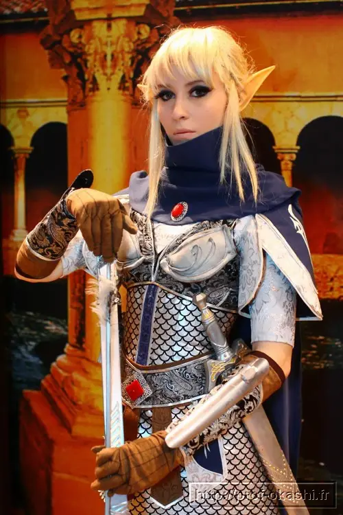 A person in detailed fantasy armor with pointed ears, holding a sword, stares directly at the camera with a deadpan…