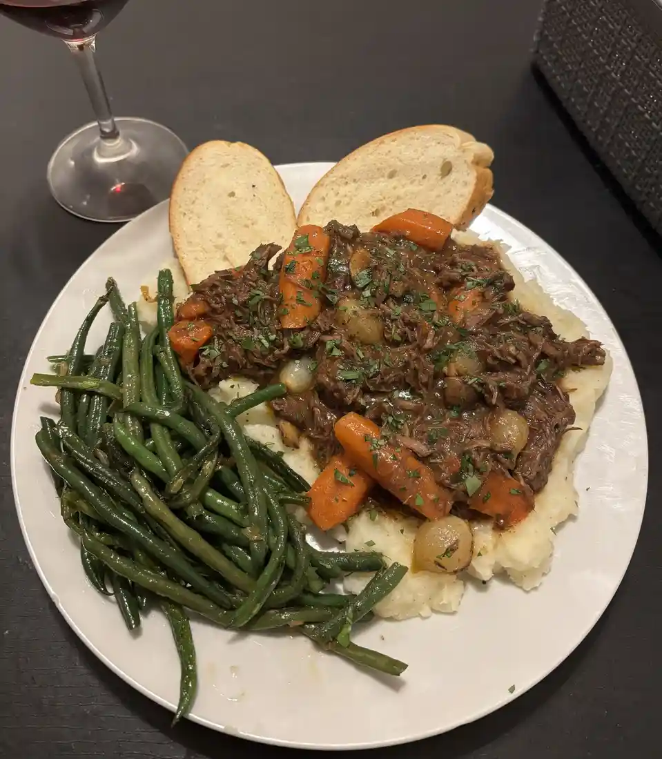 A plate of food featuring mashed potatoes topped with shredded beef stew with carrots and onions, accompanied by green beans…