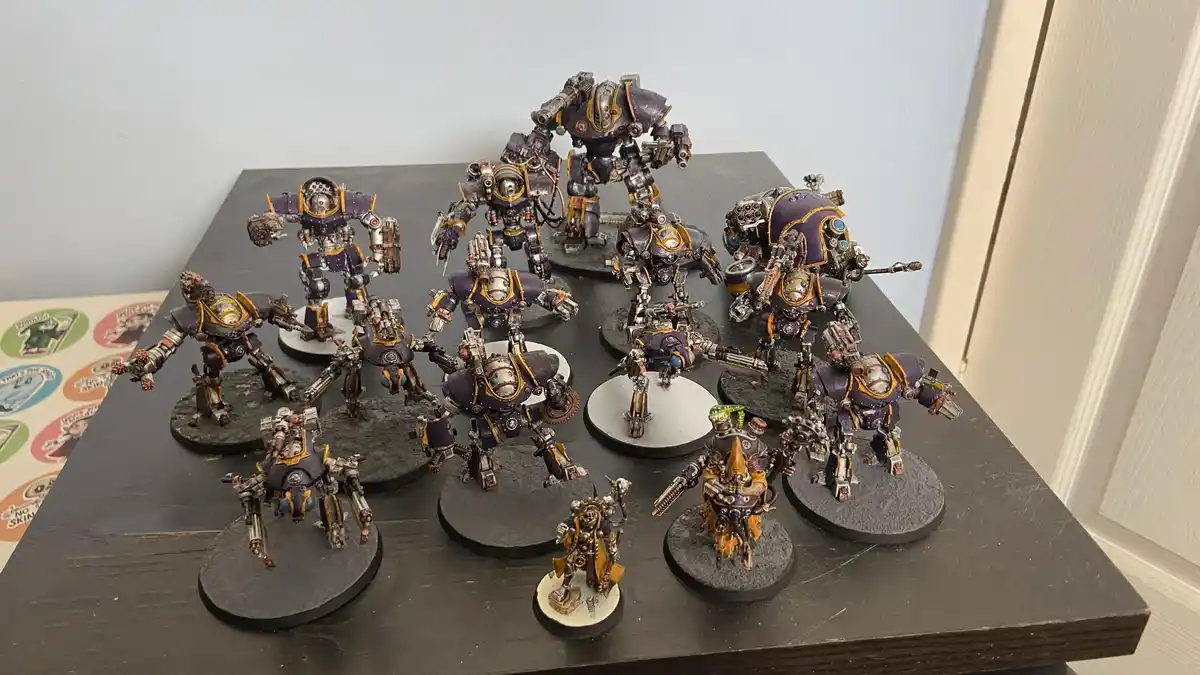 A collection of intricately painted, purple and gold armored miniature robots and figures are displayed on a dark wooden…