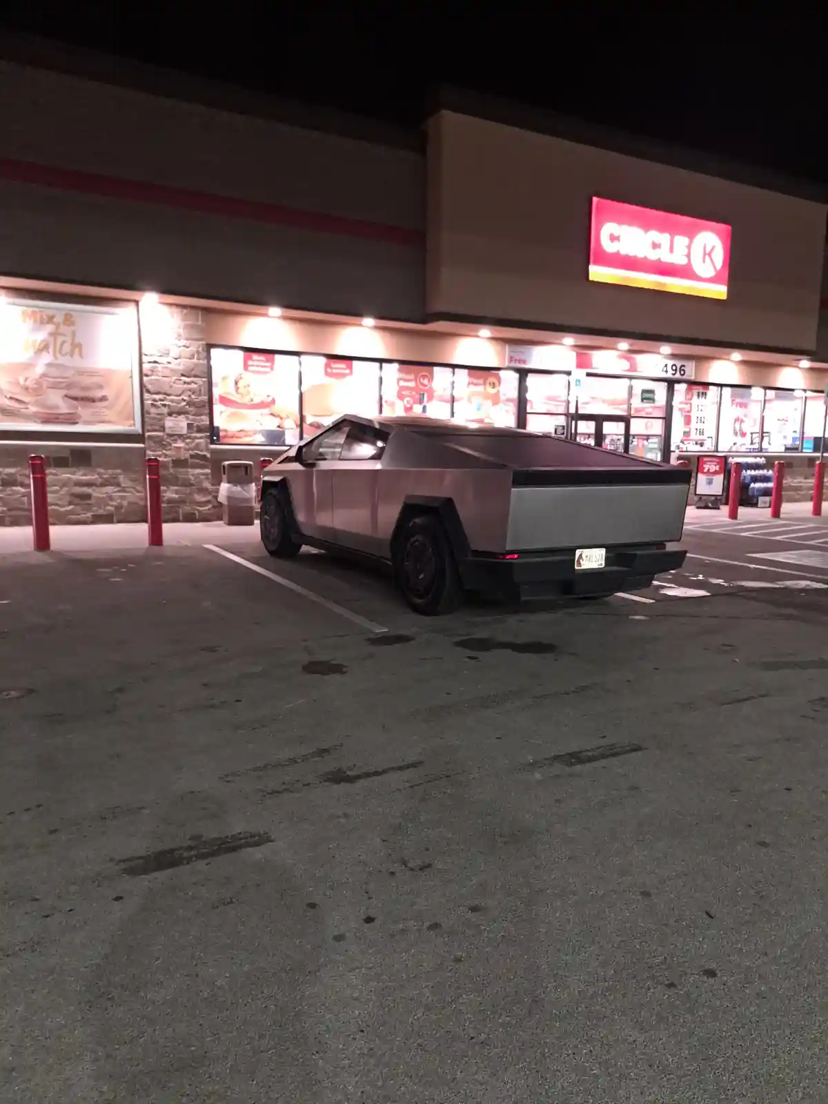 A silver Tesla Cybertruck is parked in a Circle K convenience store parking lot at night. The store's red and white sign is…