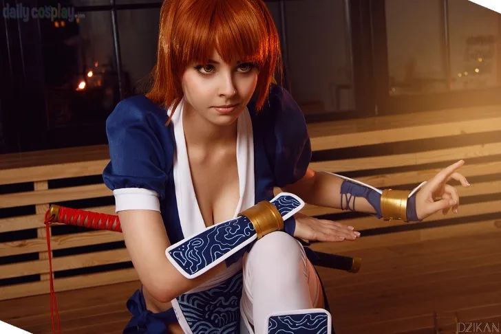 A person in a cosplay of a female anime character with orange hair, blue and white outfit, and arm guards, crouching with a…