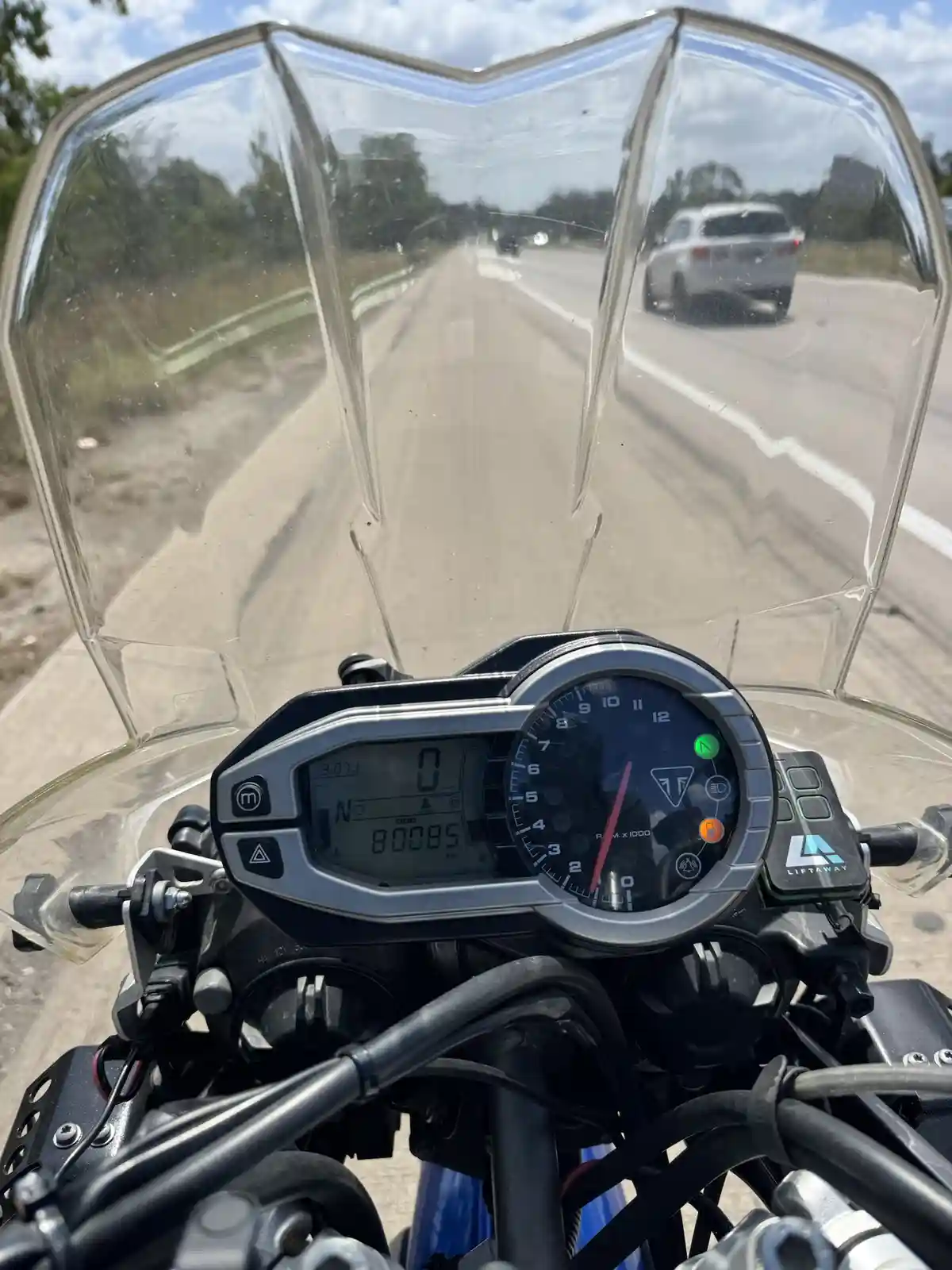 A first-person view from a motorcycle's handlebars shows a digital odometer reading 80085 km, with a speedometer at 0, while…