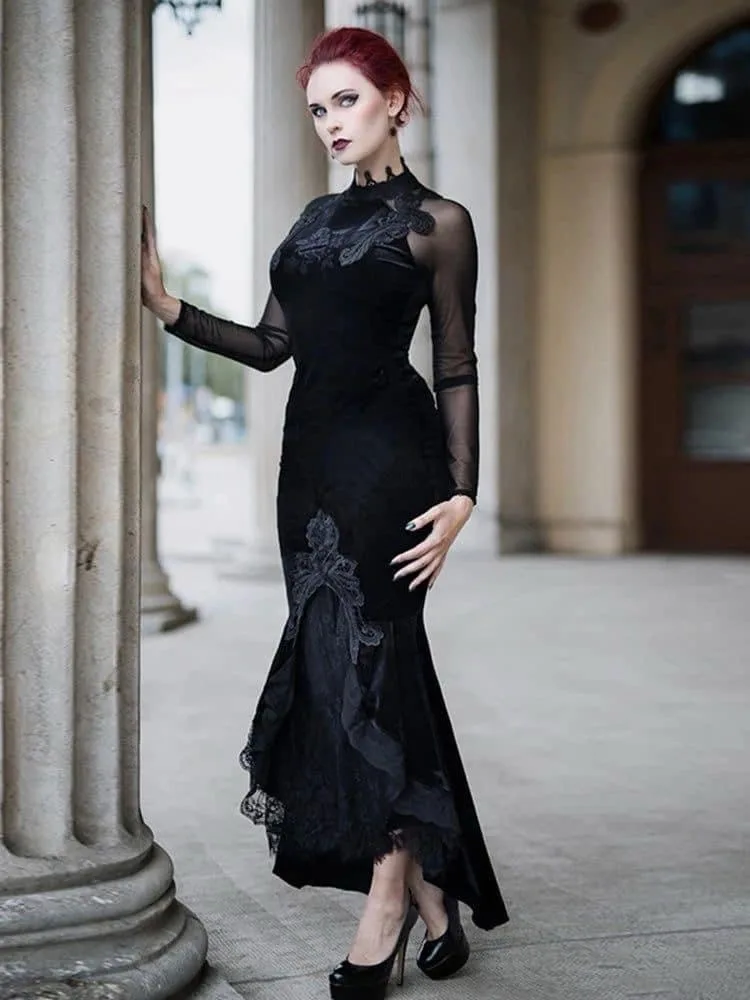 A woman with red hair and pale makeup stands leaning against a stone pillar in an ornate outdoor setting, wearing a long…