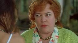 a woman with red hair and a green sweater looks at another person with a skeptical, unimpressed expression. The overlaid…