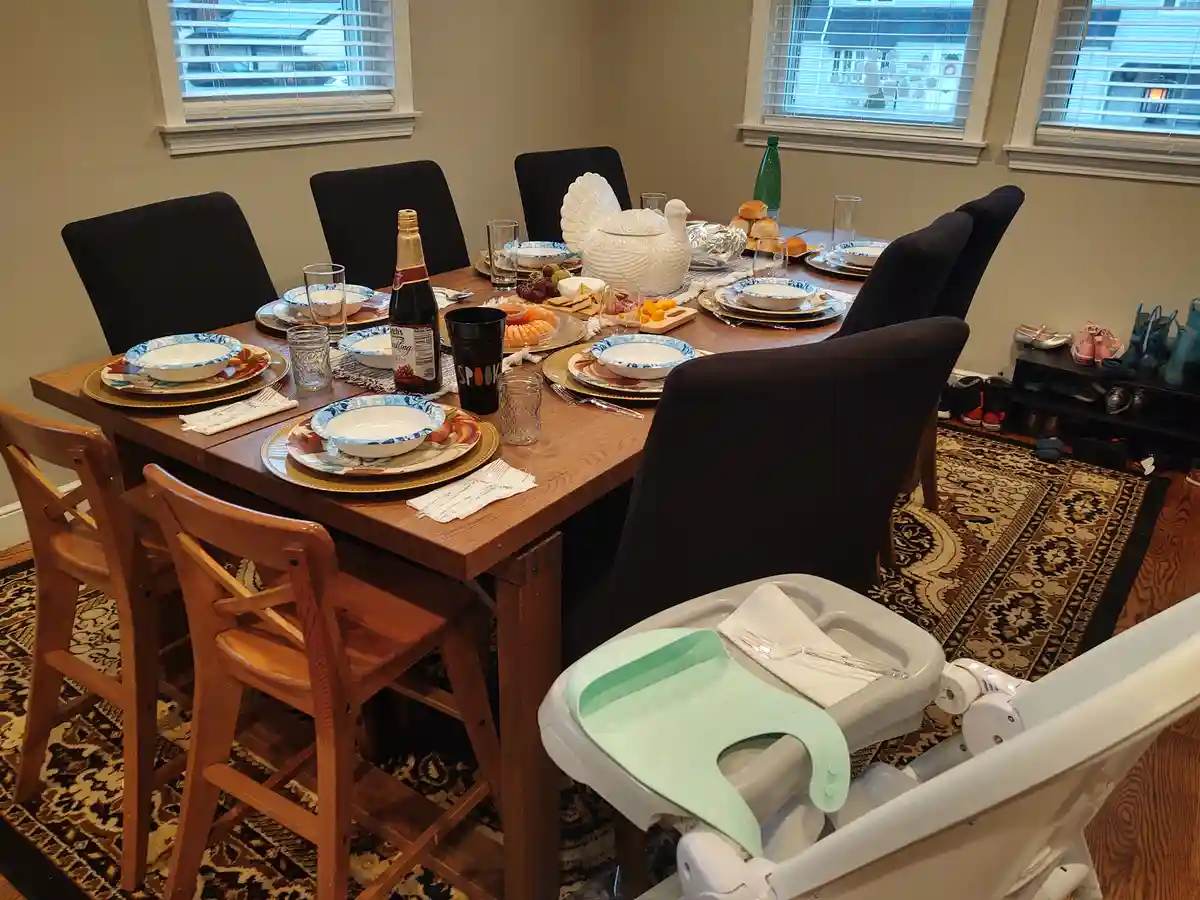 A dining table is set for a holiday meal with plates, glasses, and a turkey-shaped centerpiece, but in the foreground, an…