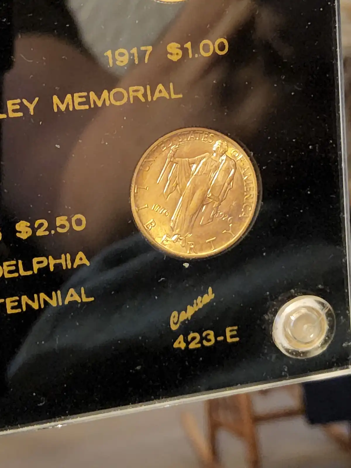 A close-up of a 1917 $1.00 gold coin displayed in a black case with gold lettering, including text like 'LEY MEMORIAL'…