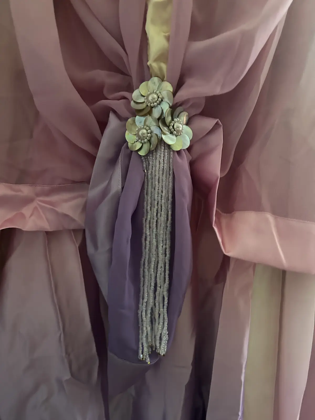 a close-up of a luxurious curtain tieback featuring pink and purple satin fabric gathered around a decorative floral…