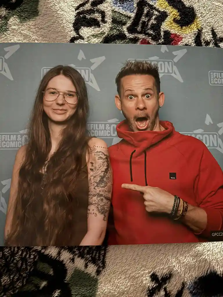 A photo of a woman with long brown hair and glasses standing next to a man in a red hoodie. The man has a surprised…