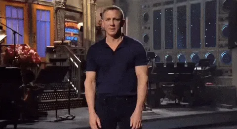A still image of actor Daniel Craig standing on a stage in a dark blue polo shirt, with overlaid text reading 'ladies and…