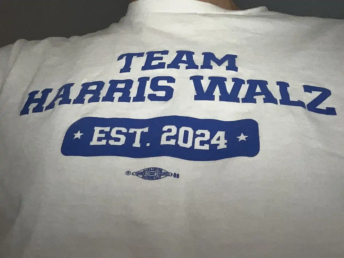 A close-up of a white t-shirt with blue text reading 'TEAM HARRIS WALZ' above a blue banner with 'EST. 2024' in white…