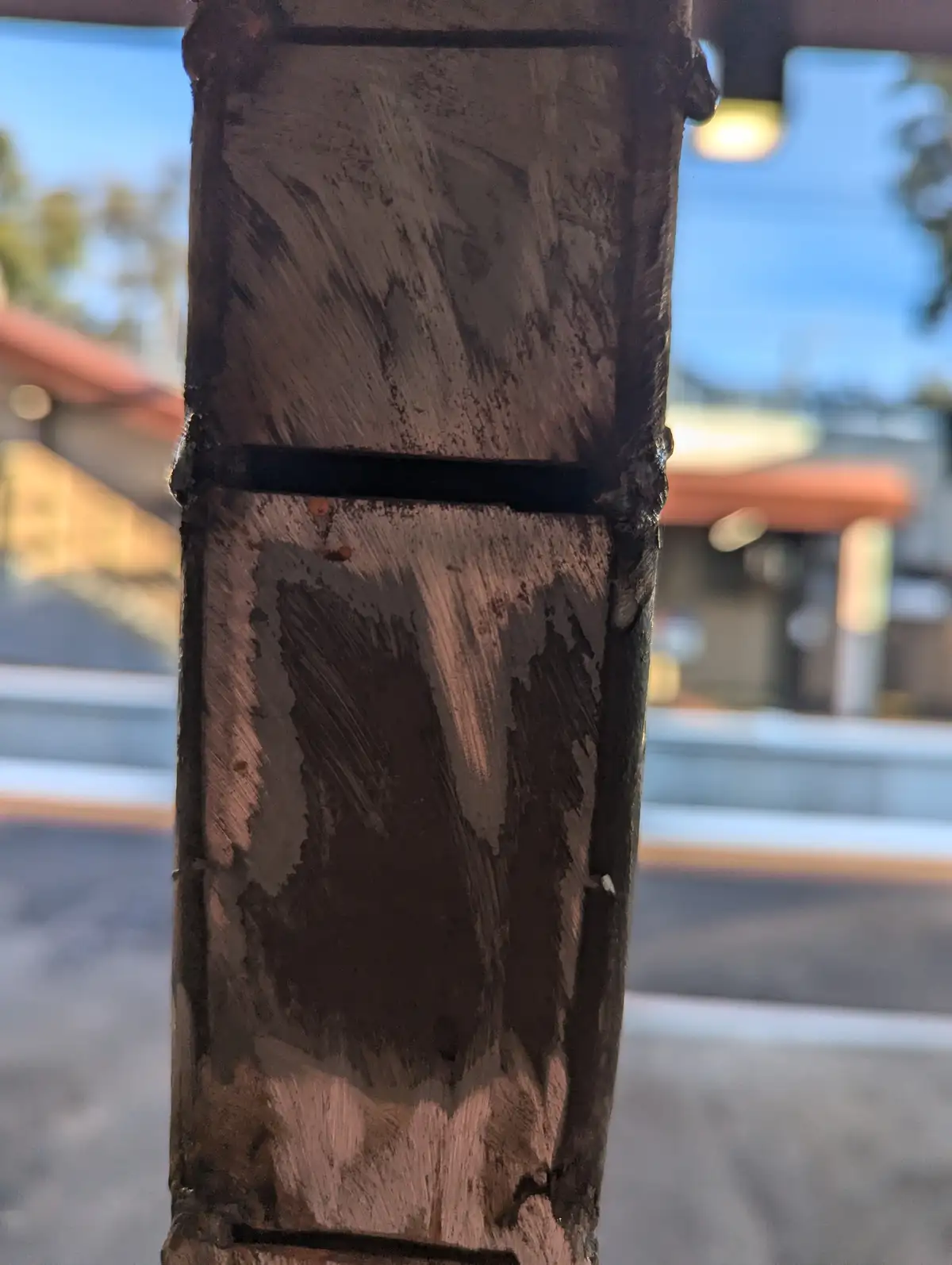 A close-up photo shows a weathered, dark brown painted metal pole with visible brush strokes and peeling paint, set against…