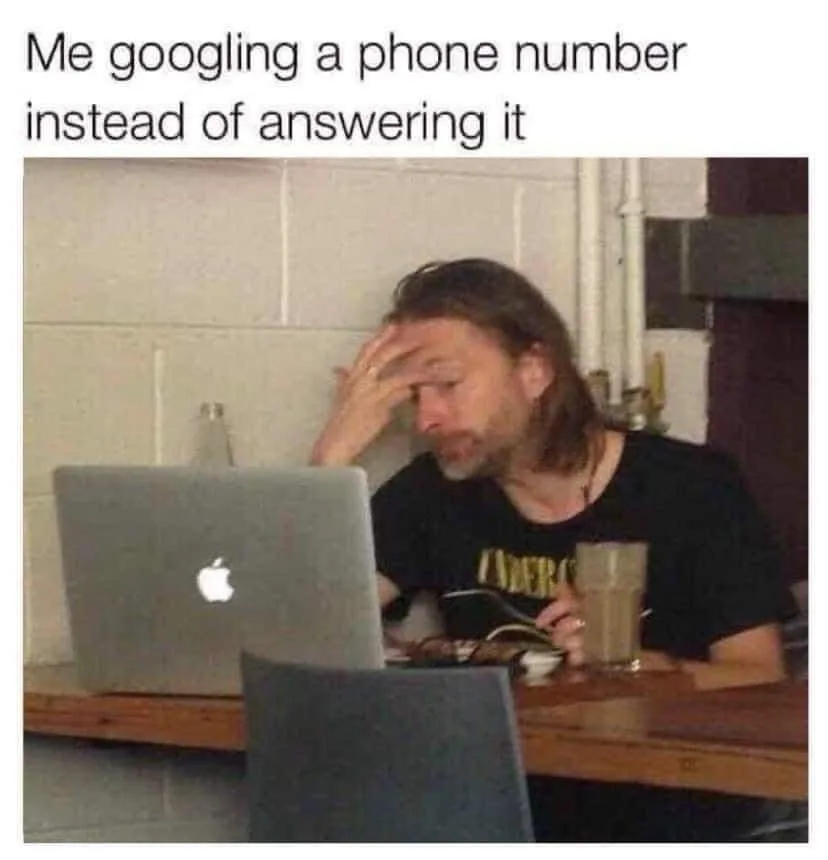 A man with long hair and a beard sits at a wooden counter, looking frustrated while holding his head with one hand. He is in…