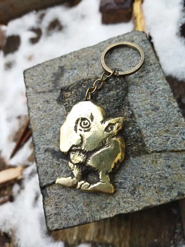 A brass keychain shaped like the character Tingle from The Legend of Zelda video games rests on a gray stone slab surrounded…