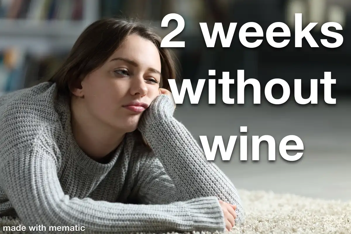 A woman in a grey knit sweater lies on a carpeted floor, resting her head on her hand with a weary, pensive expression…