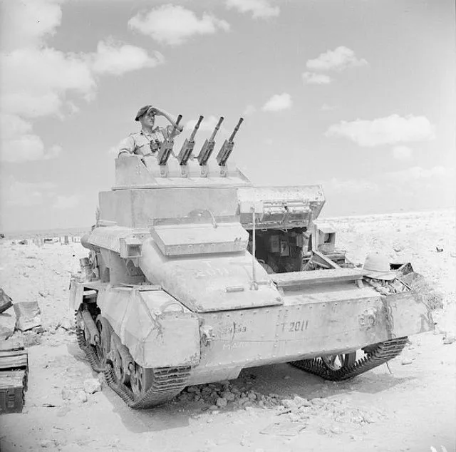 A black-and-white historical photo shows a damaged military tank in a desert landscape, with a soldier standing atop it…