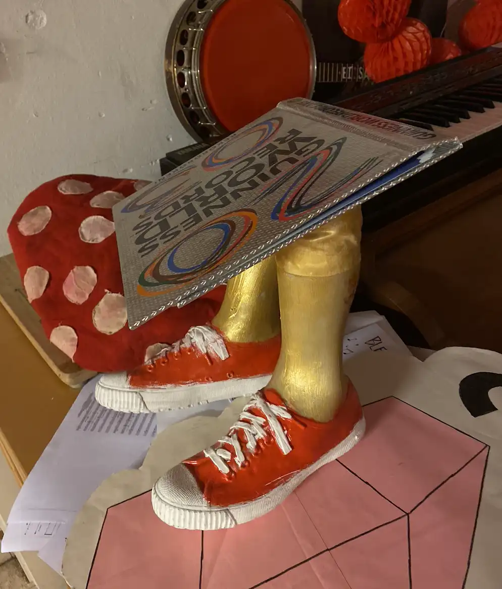 A handmade figurine with gold-painted legs and red sneakers has a Guinness World Records book balanced on its head. The…