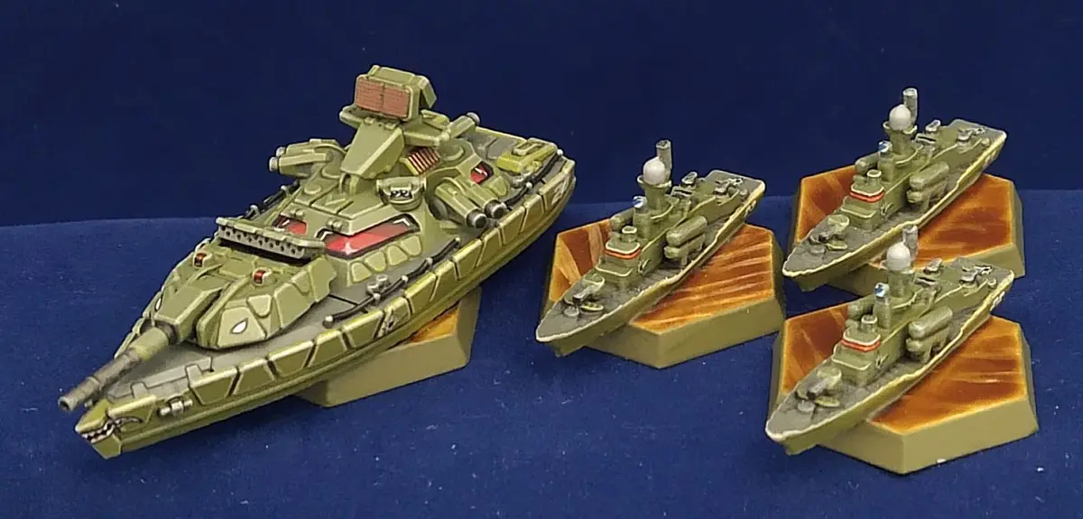 Four miniature warship models are displayed on a blue surface. One large, heavily armed warship model is positioned on the…