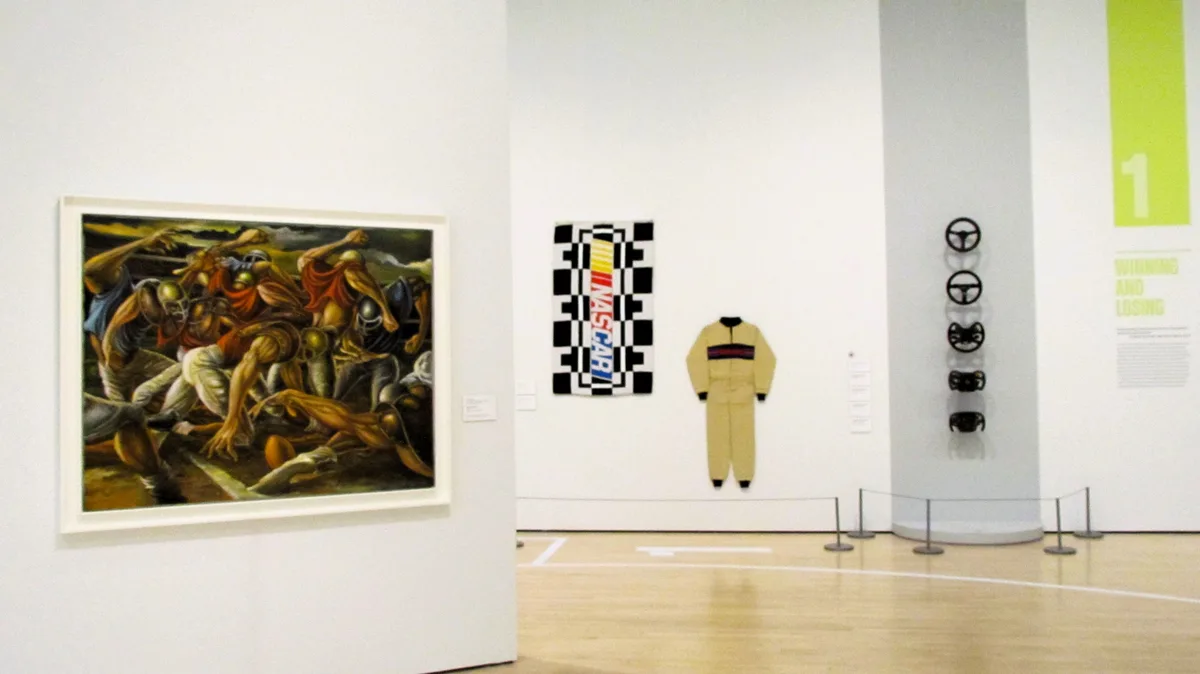 An art gallery room displays a large classical painting of muscular figures on the left, next to a checkered flag with…