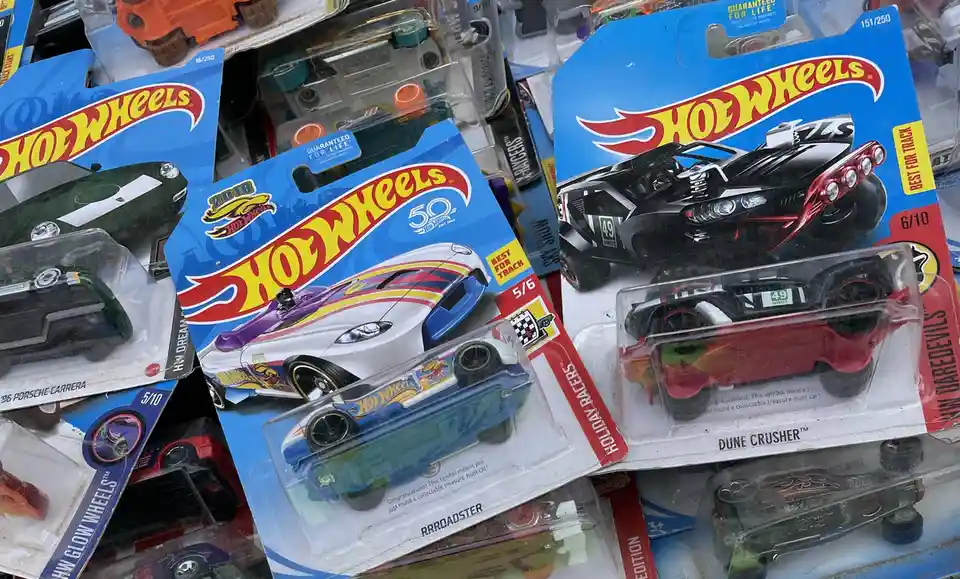 A close-up shot of several Hot Wheels toy cars in their original blister packaging, stacked and slightly overlapping. The…