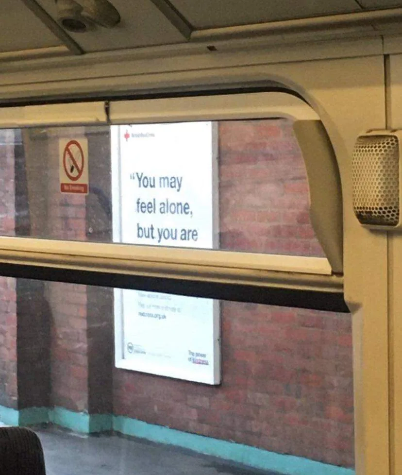 A photo taken from inside a train looking out at a station platform, showing a white advertisement poster with the text 'You…