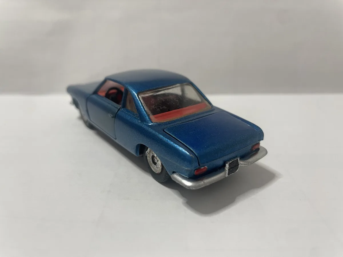 A blue toy car with red interior is photographed from a rear three-quarter angle on a plain white surface. The overlaid text…