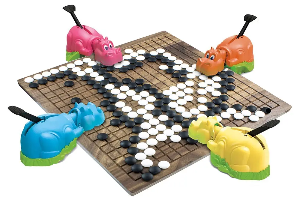four colorful plastic hippo-shaped game pieces (pink, orange, blue, yellow) sit at the corners of a wooden go board, which…