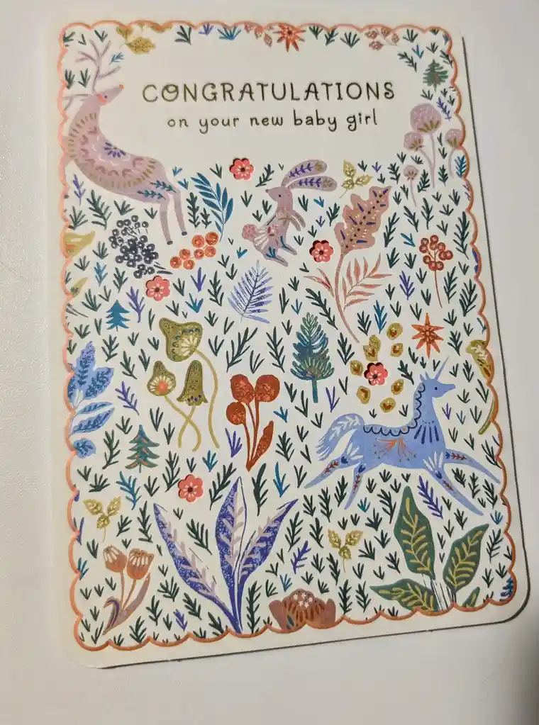 A colorful, whimsical baby congratulations card features a forest scene with stylized animals including a pink deer, a…