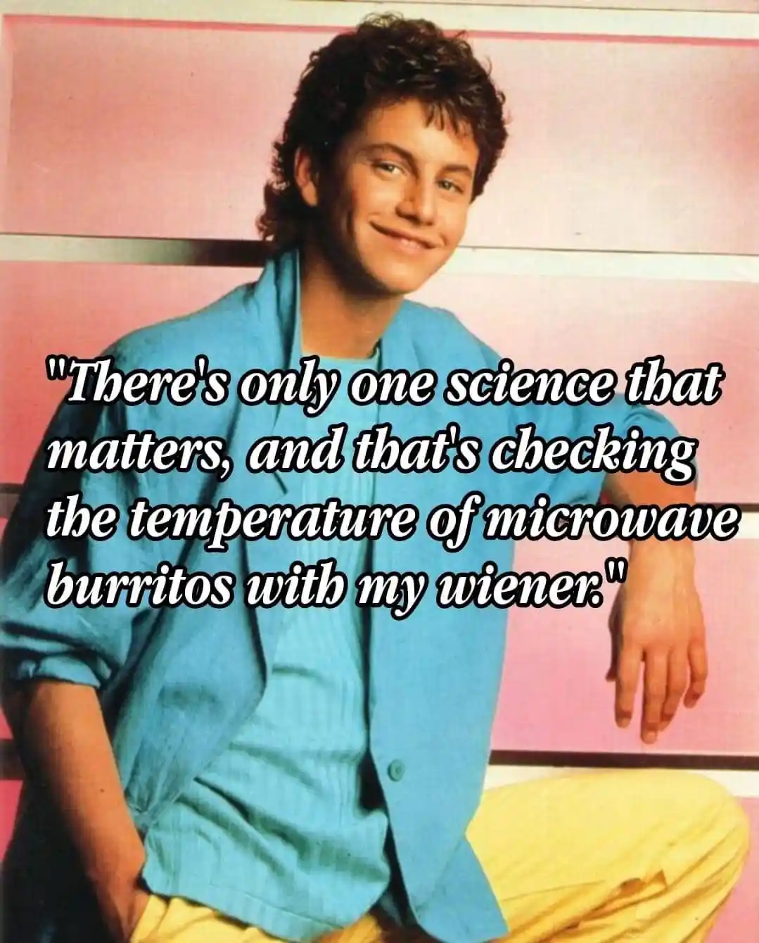 A young man with curly hair, wearing a blue shirt and yellow pants, sits against a pink and white striped background…