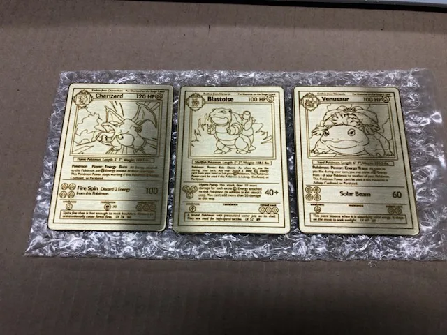 Three Pokémon trading cards—Charizard, Blastoise, and Venusaur—are laid out side-by-side on bubble wrap. Each card shows its…