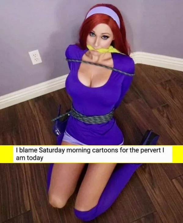 A person in a purple cosplay outfit resembling a cartoon character is kneeling on a wooden floor with their mouth covered by…