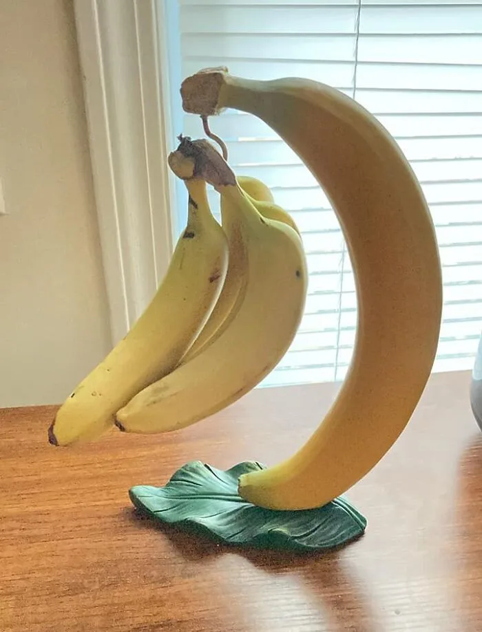 A decorative banana-shaped stand holds three real bananas, with the large curved banana forming the base and the three…