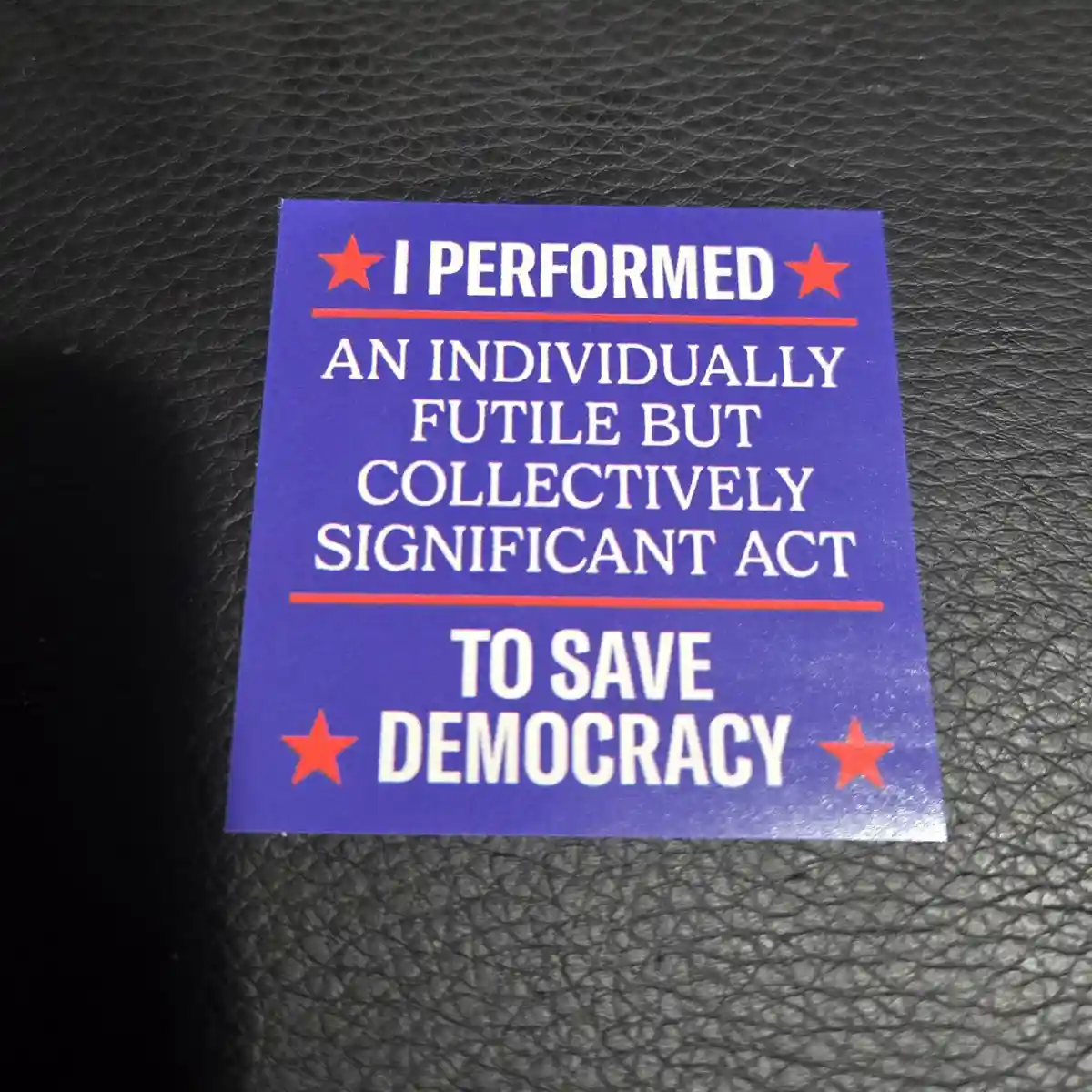 A blue sticker with white text and red stars reads 'I PERFORMED AN INDIVIDUALLY FUTILE BUT COLLECTIVELY SIGNIFICANT ACT TO…