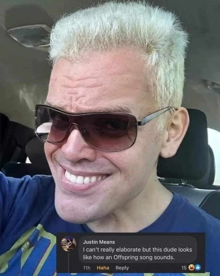 A man with platinum blonde hair and large sunglasses is smiling broadly while sitting in a car. A screenshot of a social…