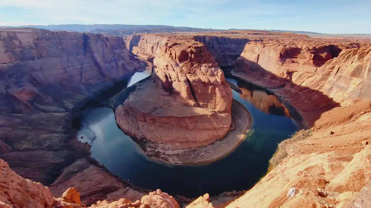 A wide-angle photograph shows the iconic horseshoe bend of the Colorado River in Arizona, with its deep blue water curving…