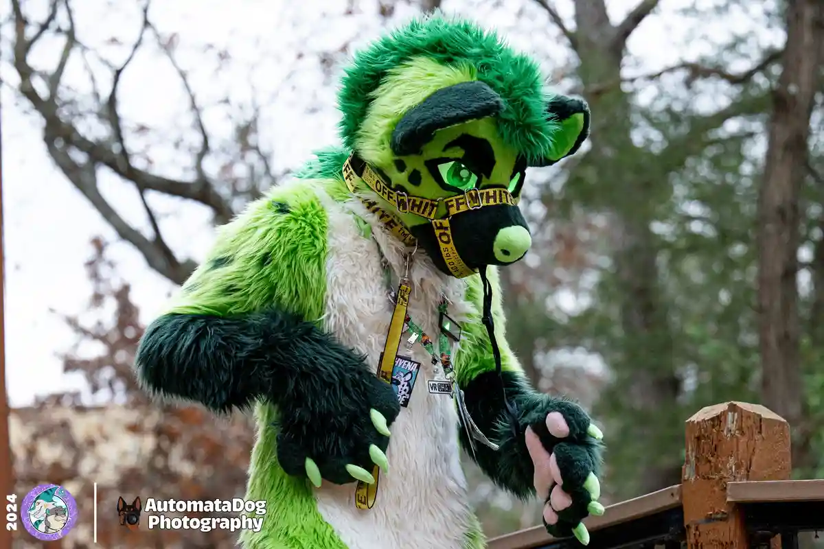 A person in a detailed green and black hyena fursuit with glowing green eyes and a yellow 'OFF-WHITE' branded muzzle stands…