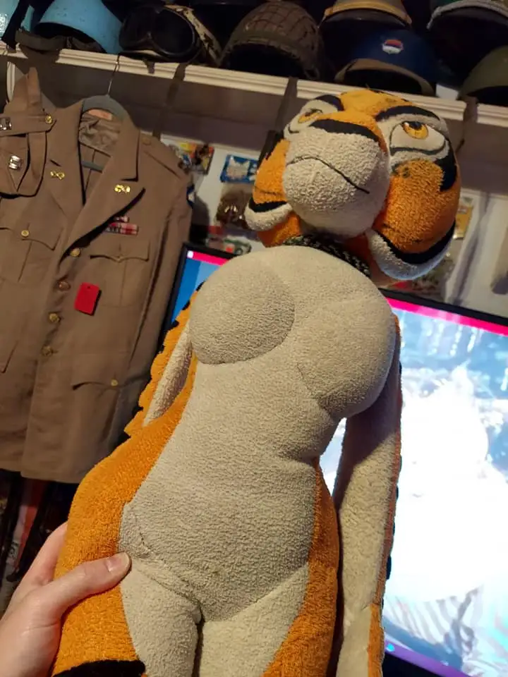 A person holds a large tiger plushie from behind, showing its backside which has been sewn to resemble a human torso with…