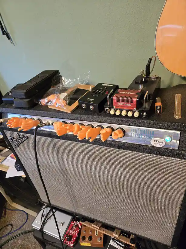 A Fender Bandmaster Reverb-Amp is shown with multiple small orange plastic hands attached to its knobs, as if they are…