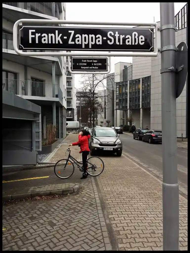 A street sign reading 'Frank-Zappa-Straße' with a plaque below it detailing Frank Zappa's birth and death dates and his…