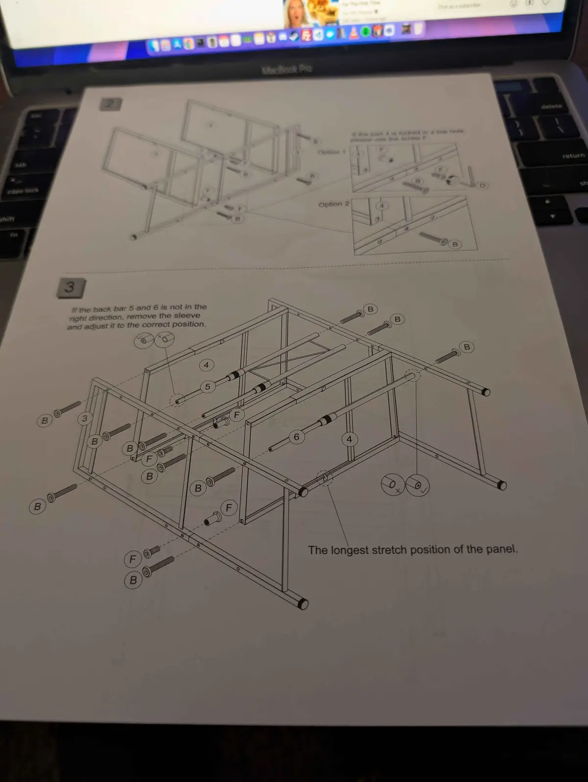 A close-up photo shows a printed furniture assembly manual resting on a laptop keyboard. The manual displays technical line…