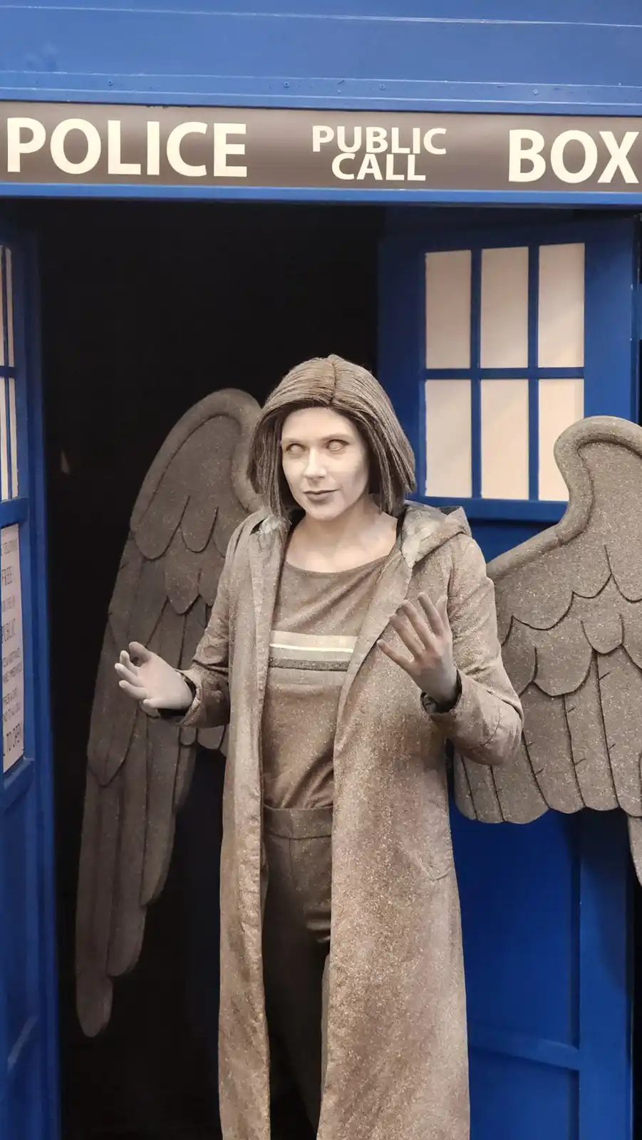 A person dressed as the Weeping Angel from Doctor Who, with large stone-like wings and a glittery brown outfit, stands in…