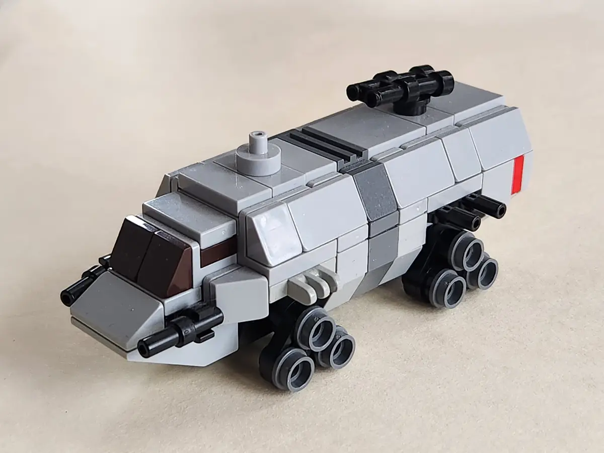 A gray Lego model of a futuristic armored vehicle with black treads, mounted cannons, and a red stripe, sits on a beige…