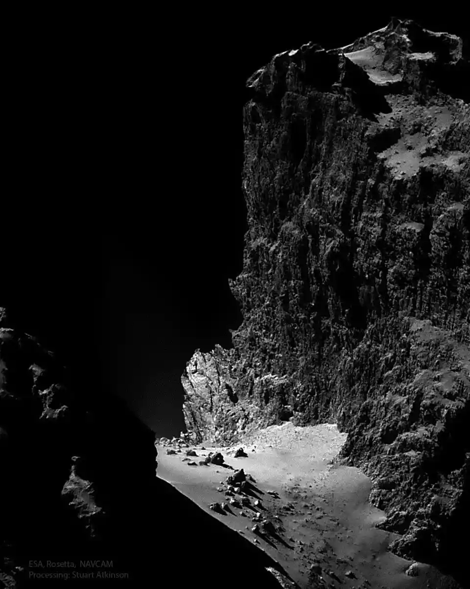 a black and white photograph of a rugged, rocky terrain with a steep cliff on the right and a dark void on the left…