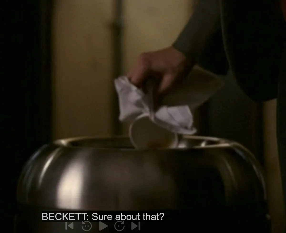 A close-up shot shows a person's hand dropping a crumpled white paper into a large, shiny metal bowl. The image has a dark…