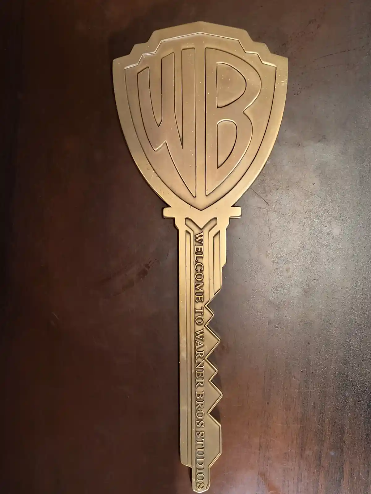 A golden key-shaped souvenir with the Warner Bros. shield logo at the top and the text 'WELCOME TO WARNER BROS STUDIOS'…