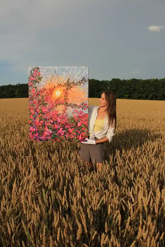 A woman stands in a golden wheat field holding a large, colorful painting of a vibrant sunset with pink and orange flowers…