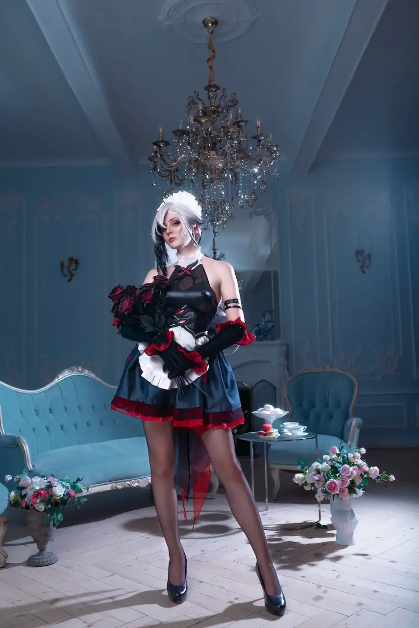 A person in a maid outfit with black gloves and a white frilly headpiece stands in a luxurious blue room with ornate…