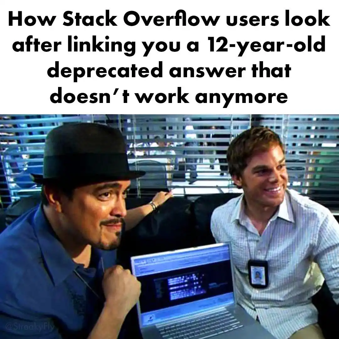 Two men sit at a laptop; one wears a black fedora and looks smugly at the camera, while the other smiles broadly. The text…