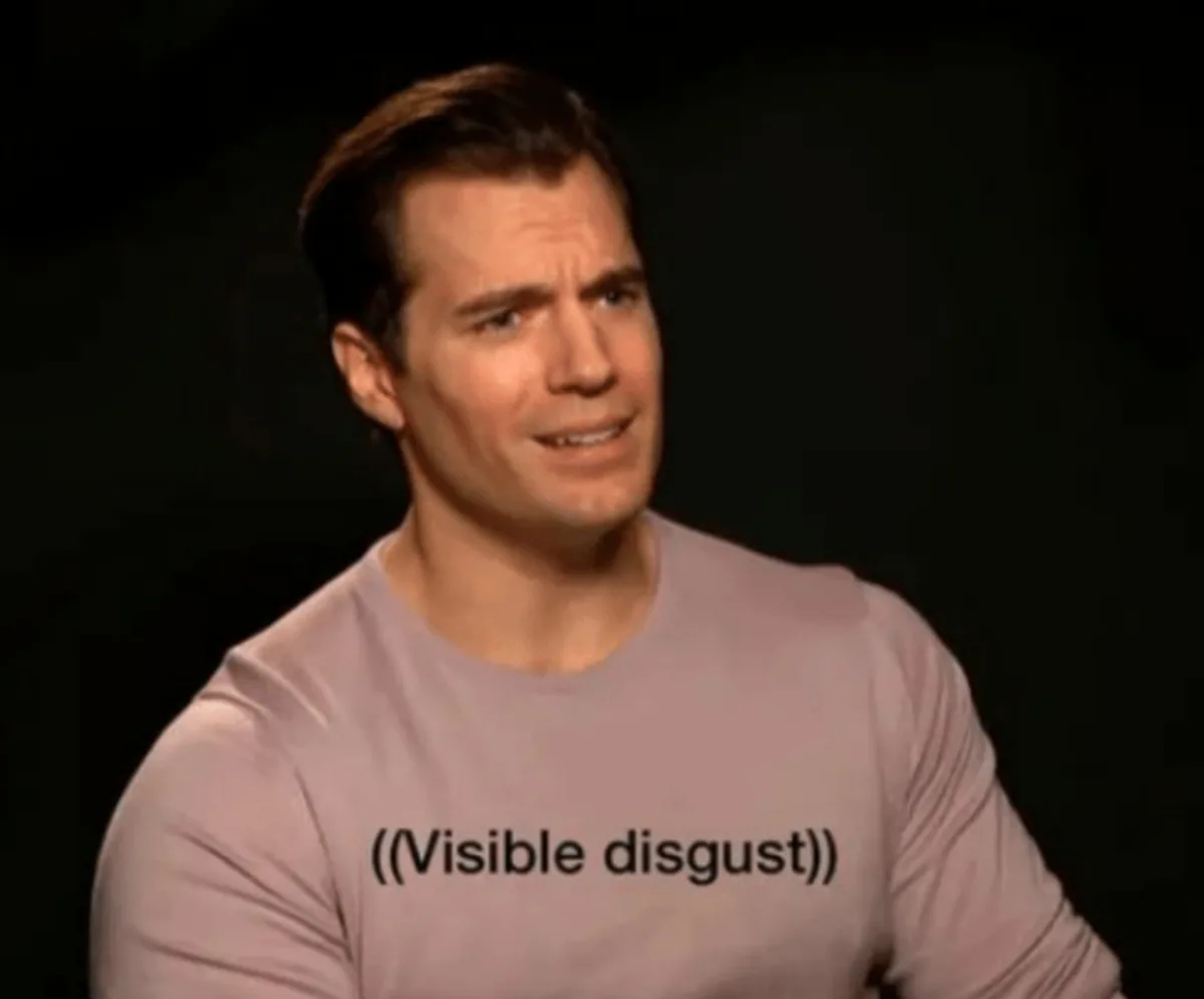A man with dark hair and a light-colored long-sleeved shirt is shown against a dark background, his face contorted in a…