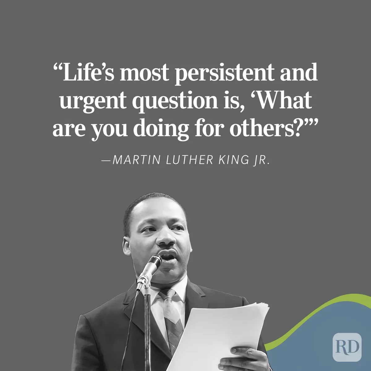 A black and white photo of Martin Luther King Jr. speaking into a microphone while holding papers. Overlaid text quotes him…